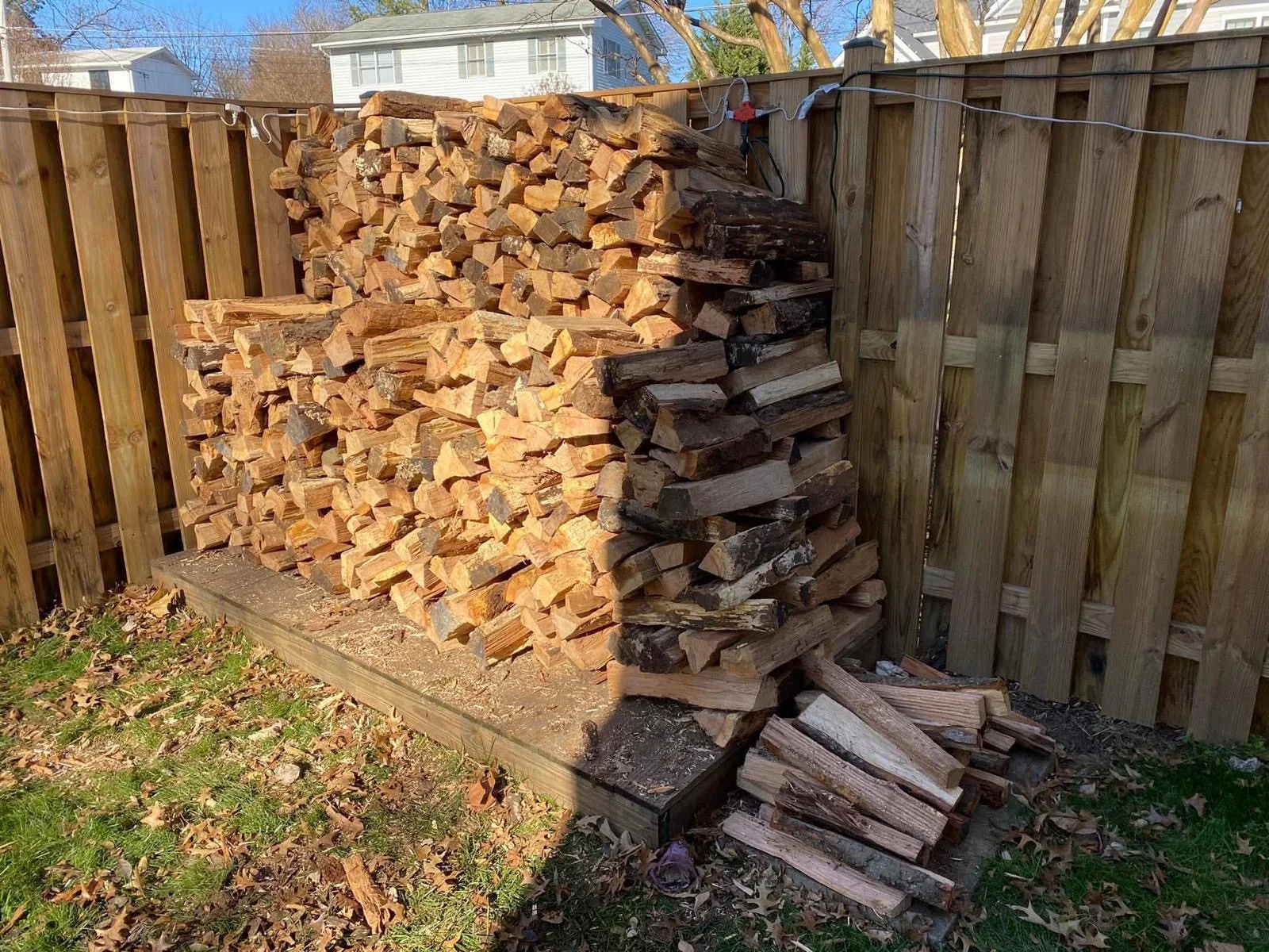 Split firewood stacked outdoors beside a wooden fence